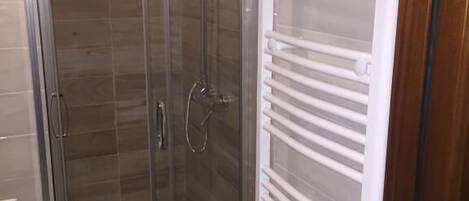 A glass-enclosed shower area with a white towel rack beside it.