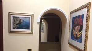 A hallway with two framed paintings on the walls, a tiled floor, and an arched doorway leading to another room. - B&B Lumasa (Vietri sul Mare)