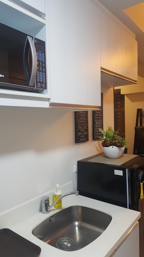 Compact kitchen area with a stainless steel sink, modern refrigerator, and microwave, offering a convenient space for meal preparation.