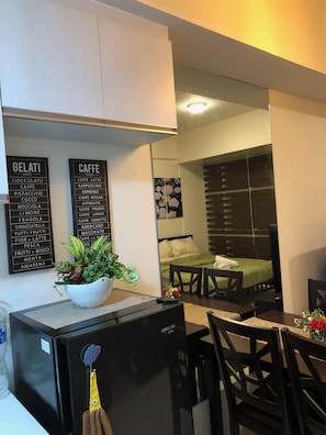 Compact kitchenette with refrigerator, dining table, and comfortable bed.