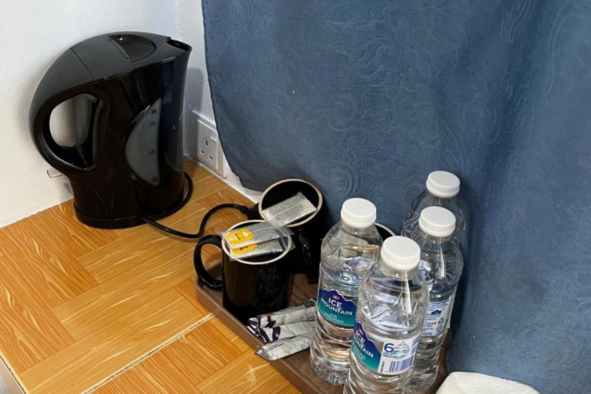 Ein Holztisch mit einer schwarzen Kaffeemaschine, einer schwarzen Tasse, zwei Wasserflaschen und einer Toilettenpapierrolle.
