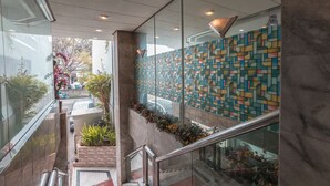 A modern interior with a glass railing, a patterned wall, and a staircase leading to an outdoor area with plants. - OYO 671 Hotel Capitol (Jakarta)