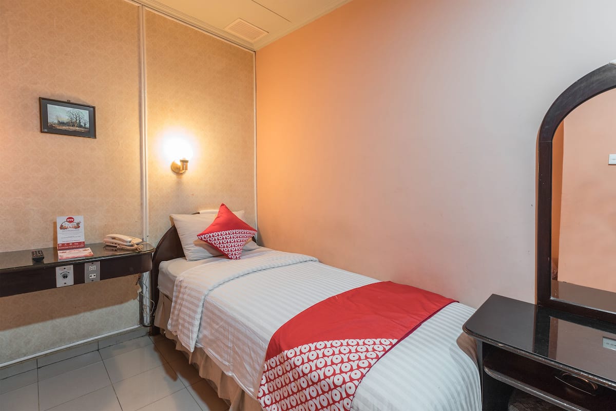 A hotel room with a bed, a bedside table with a lamp, a mirror, and a wall-mounted picture.
