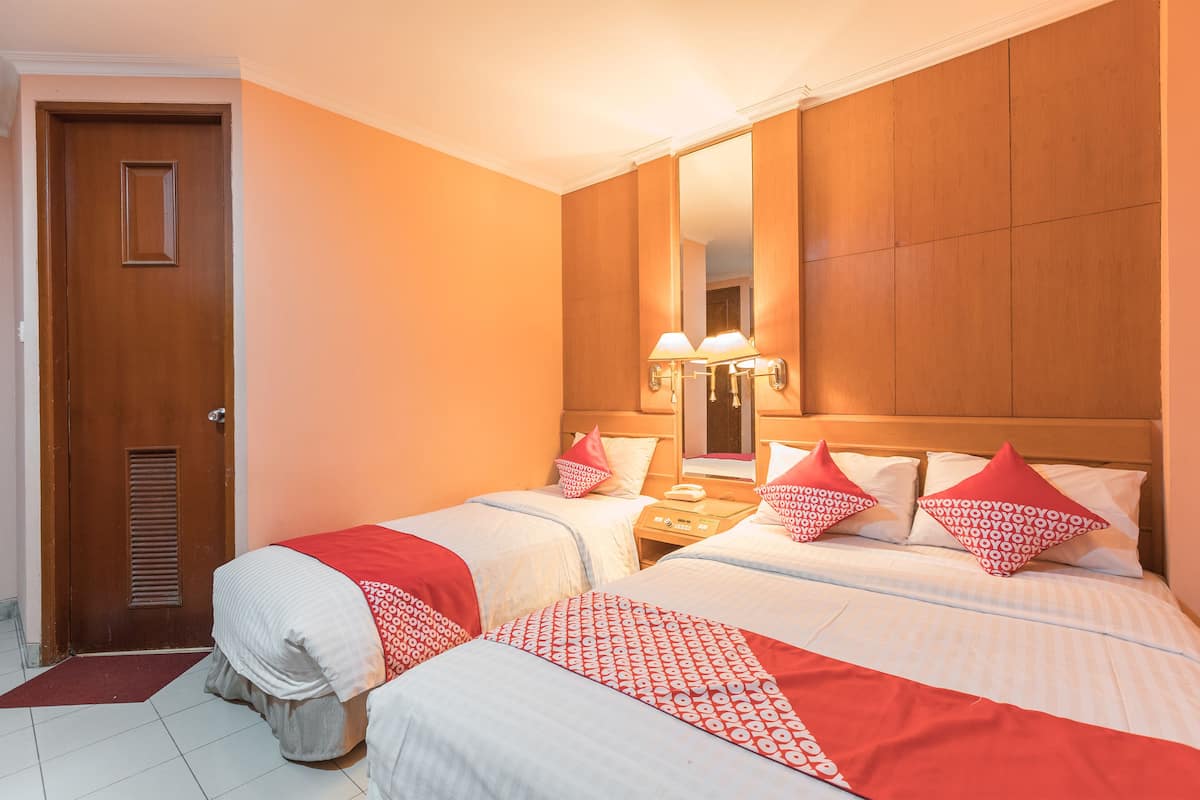 A hotel room with two beds, a wooden headboard, a nightstand with a lamp, and a mirror.