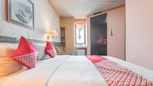 A hotel room with a bed, pillows, a lamp, a framed picture on the wall, and a door. - OYO 671 Hotel Capitol (Jakarta)