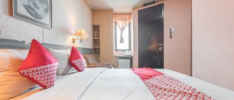 A hotel room with a bed, pillows, a lamp, a framed picture on the wall, and a door.