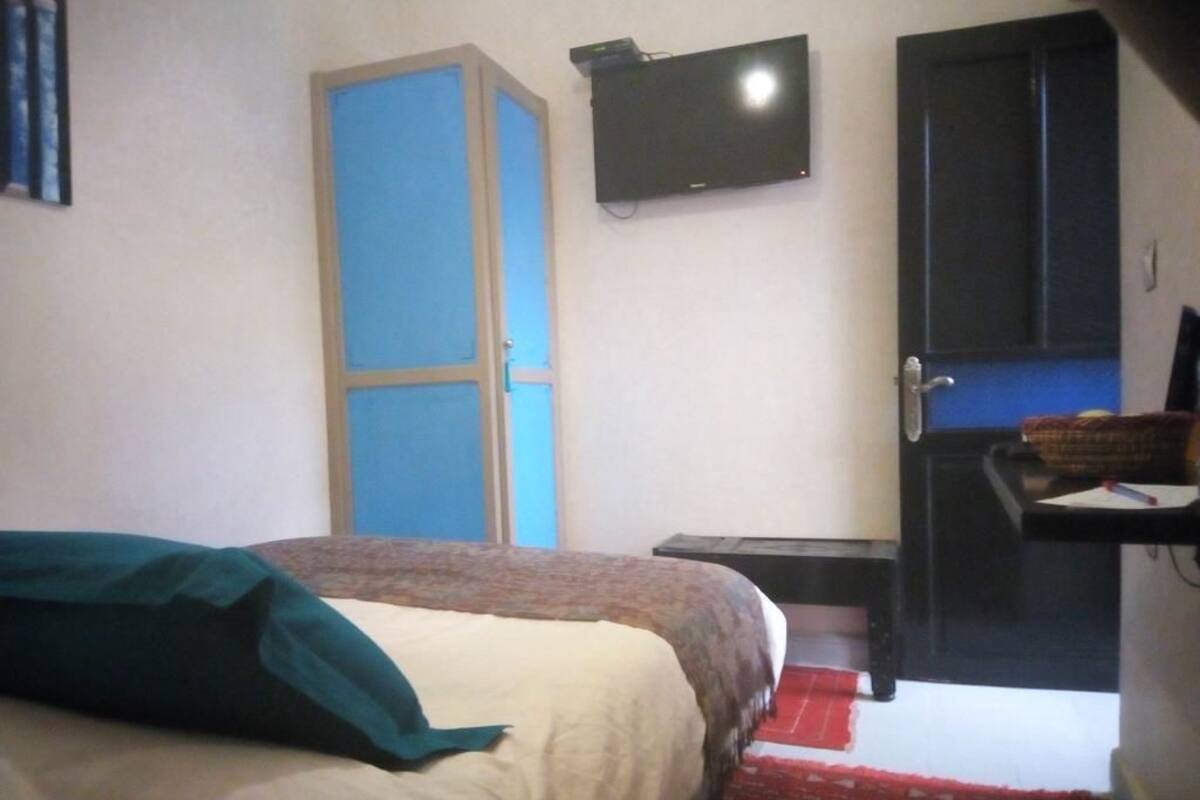 A bedroom with a bed, a television mounted on the wall, a wardrobe, and a desk with a chair.