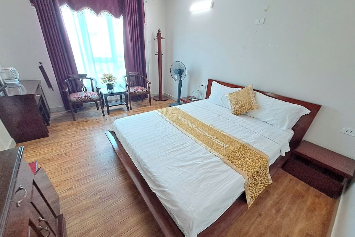 Ein Hotelzimmer mit einem großen Bett, Holzboden, einem Schreibtisch mit Stuhl, einem kleinen Tisch mit Stühlen und einem Standventilator.