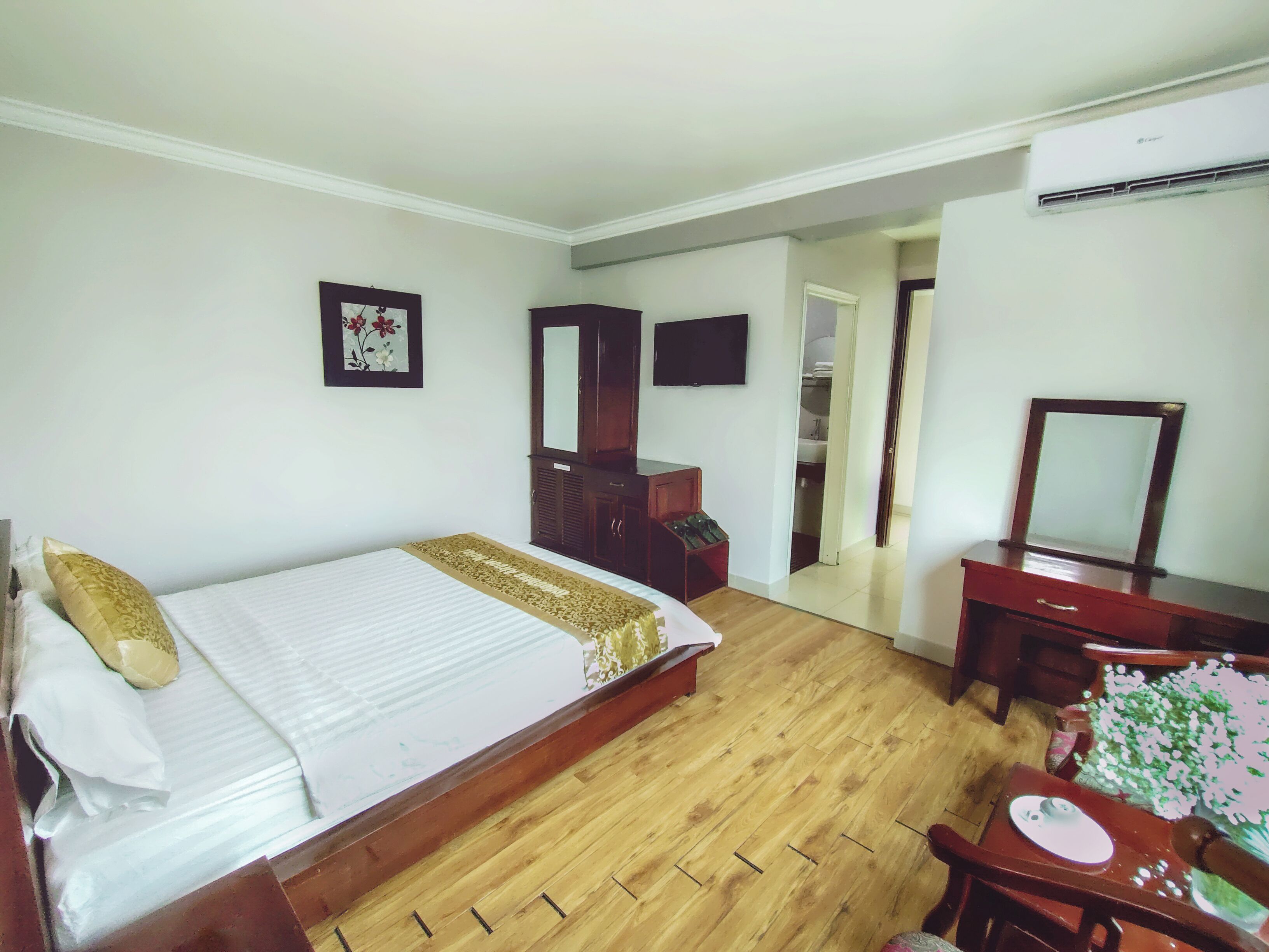 A hotel room with a bed, a wooden dresser, a desk, a mirror, a television, and a wardrobe.