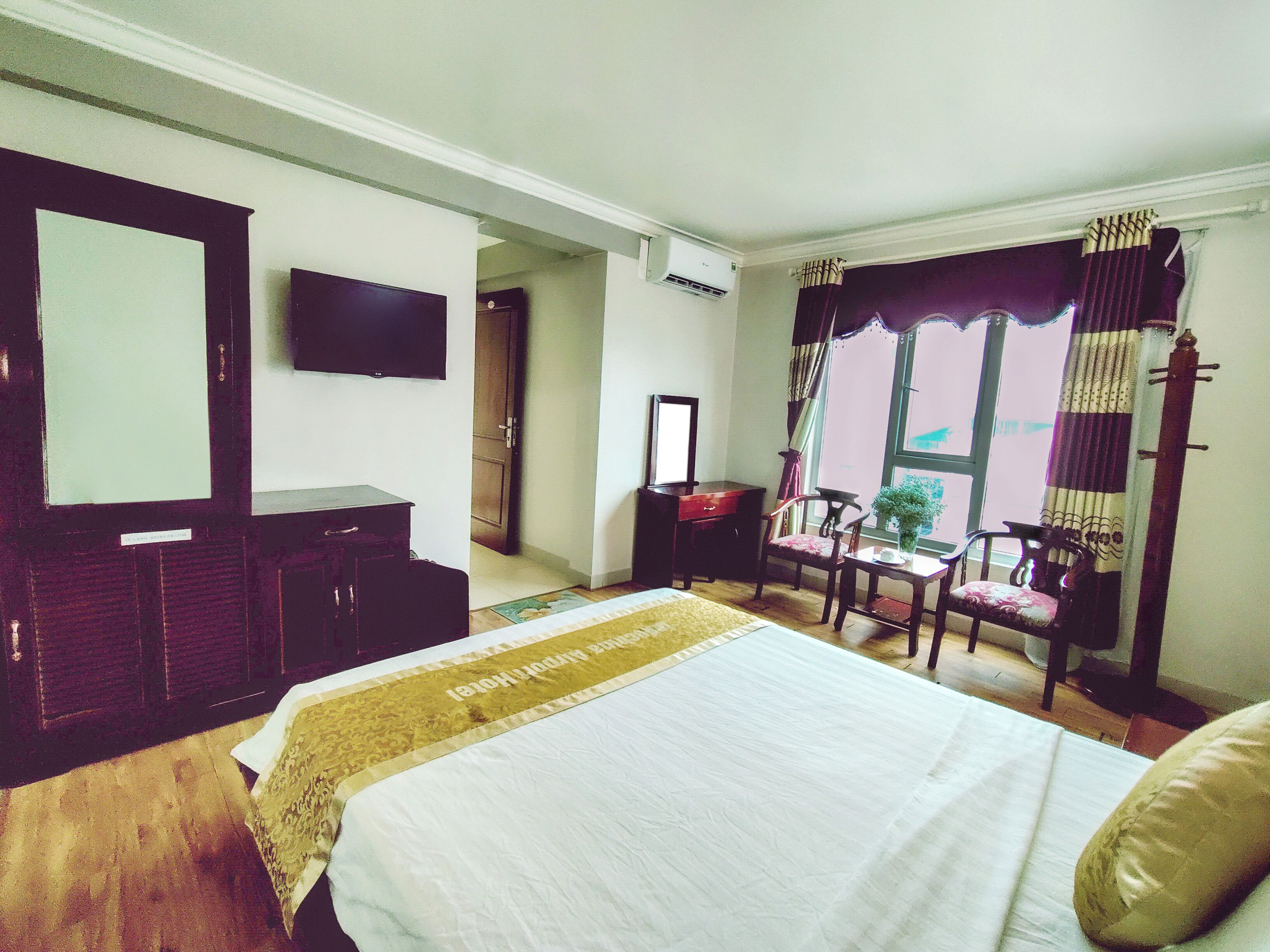 A hotel room with a bed, a desk, a chair, a TV, and a window with curtains.