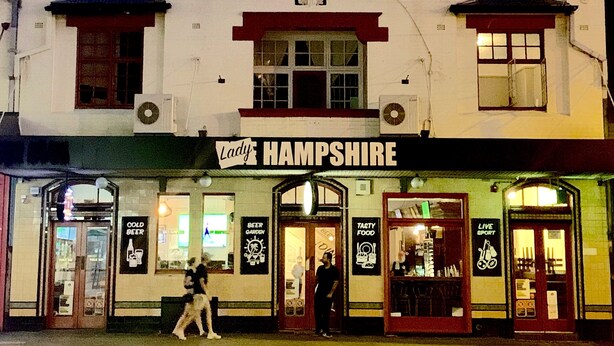 Un pub llamado "Lady Hampshire" con fachada tradicional, varias ventanas y un letrero que anuncia jardín de cerveza y deportes en vivo.