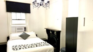 Un dormitorio con una cama, un armario negro, una ventana con persianas, un radiador y una araña.
