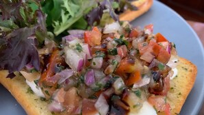 Primer plano de una bruschetta cubierta con tomate, cebolla y hierbas picadas, servida en un plato con una ensalada.