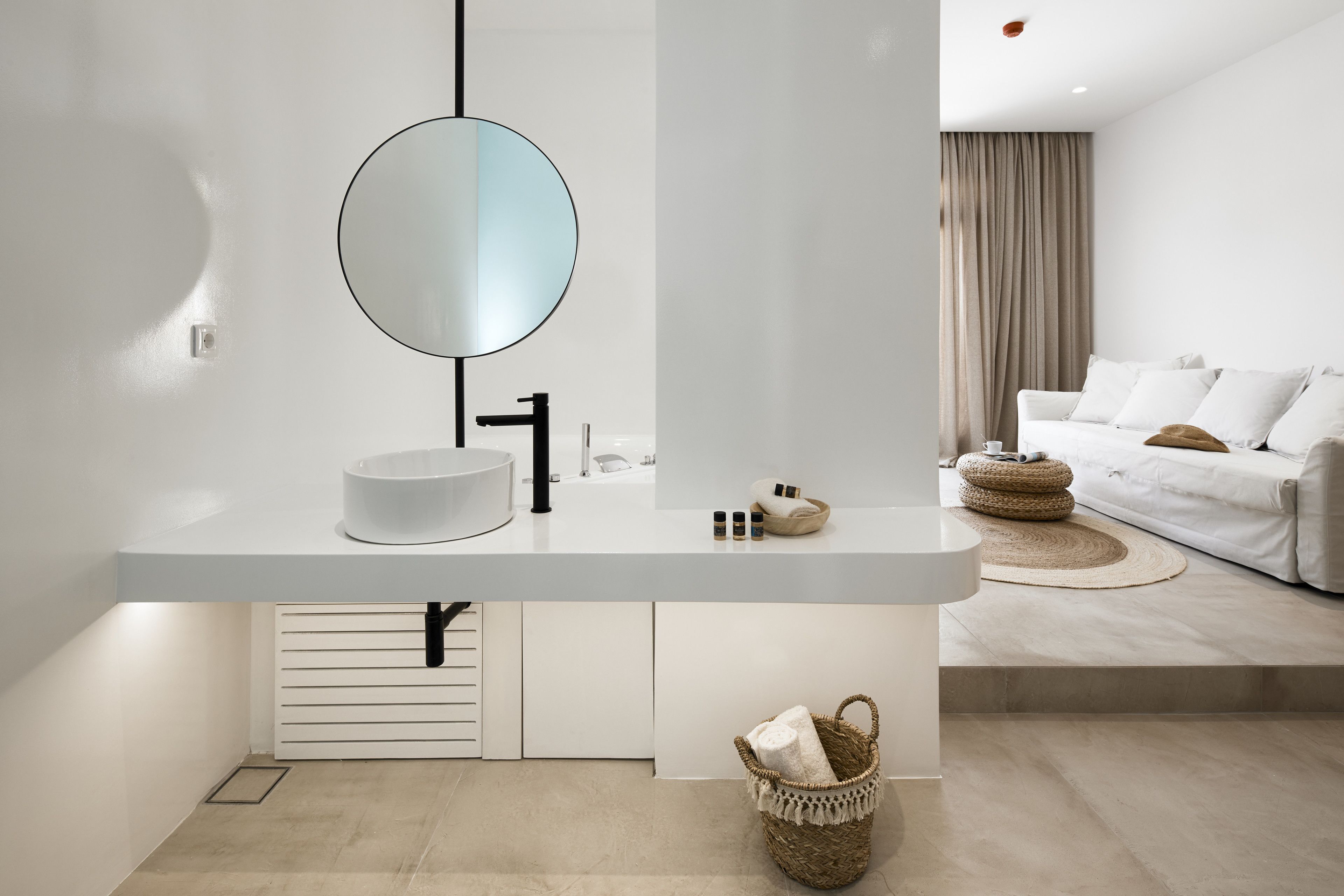 Ein modernes Badezimmer mit rundem Spiegel, weißem Waschbecken und einem kleinen Korb mit Handtüchern.