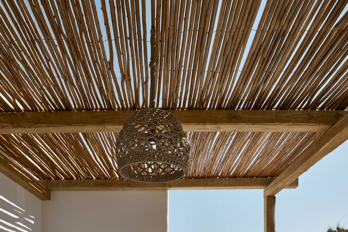 A sunlit balcony with a wooden pergola, a dining table set with breakfast, and a view of the city and mountains.