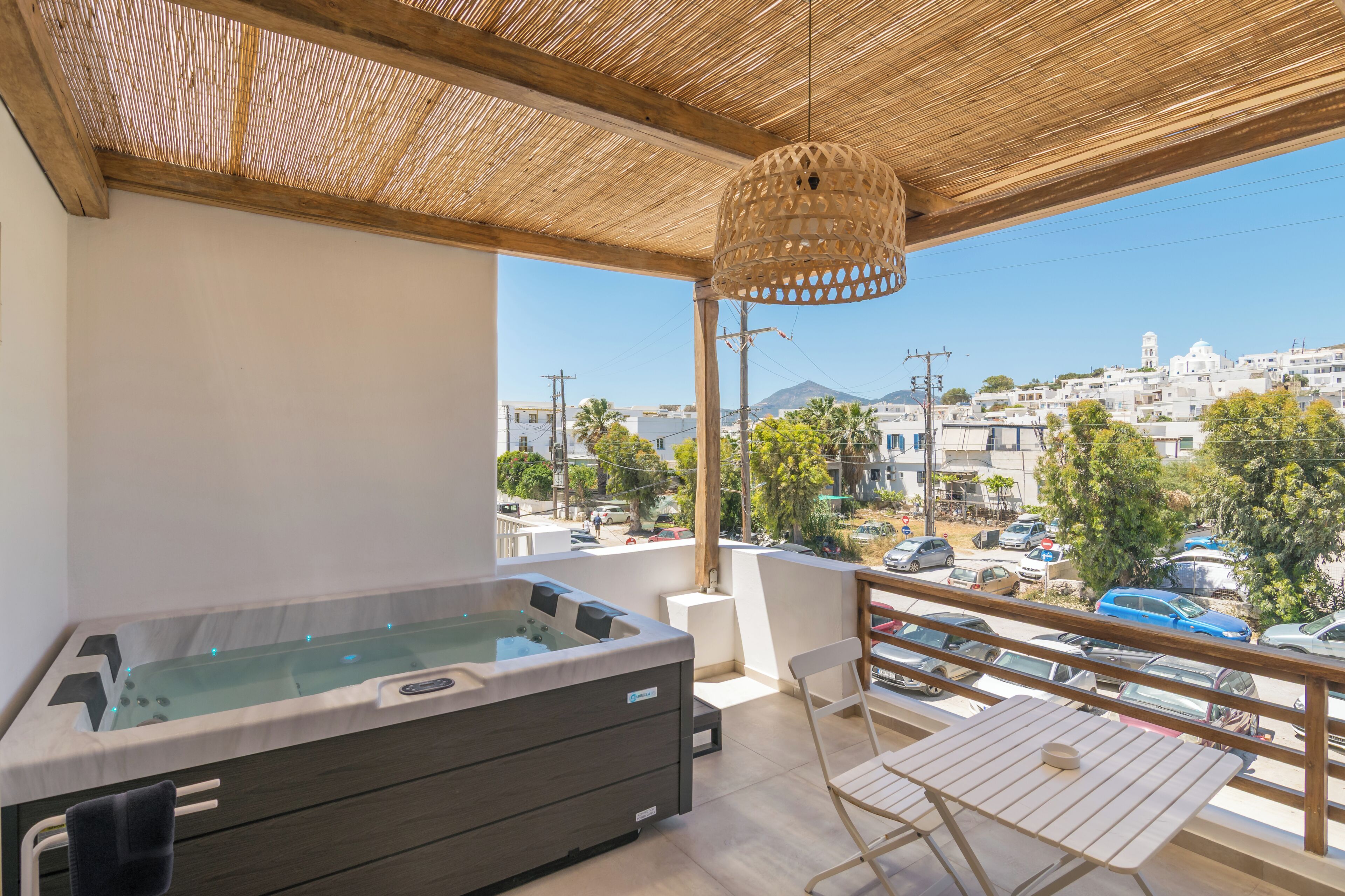 A balcony with a hot tub, a wicker hanging light fixture, and a view of a cityscape with buildings and cars.