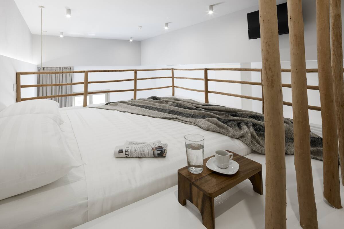 A modern bedroom with a wooden headboard, a neatly made bed, a bedside table with a glass of water and a cup, and a newspaper.