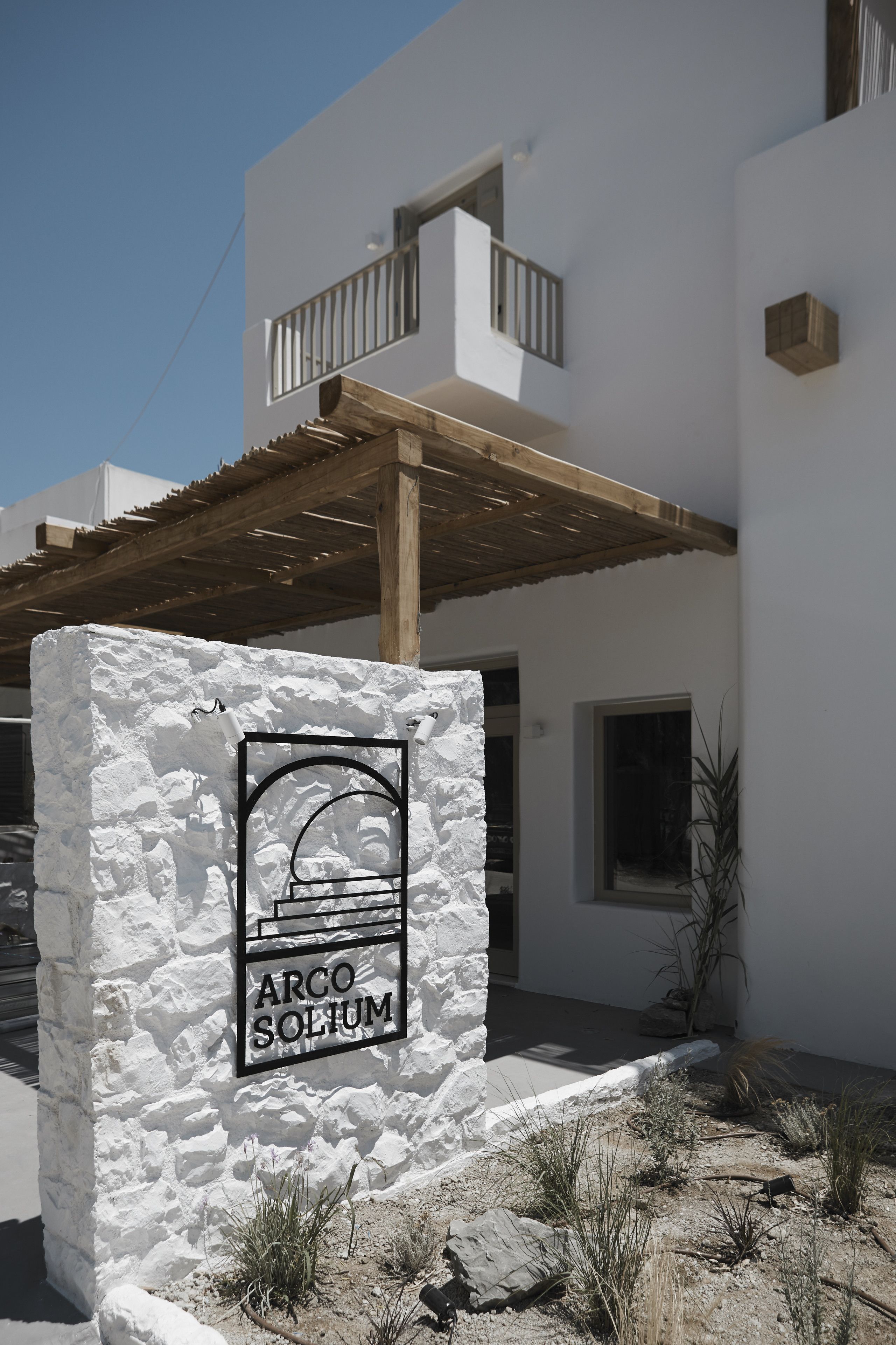 Un bâtiment blanc avec une enseigne indiquant « ARCO SOLIUM » et une pergola en bois.