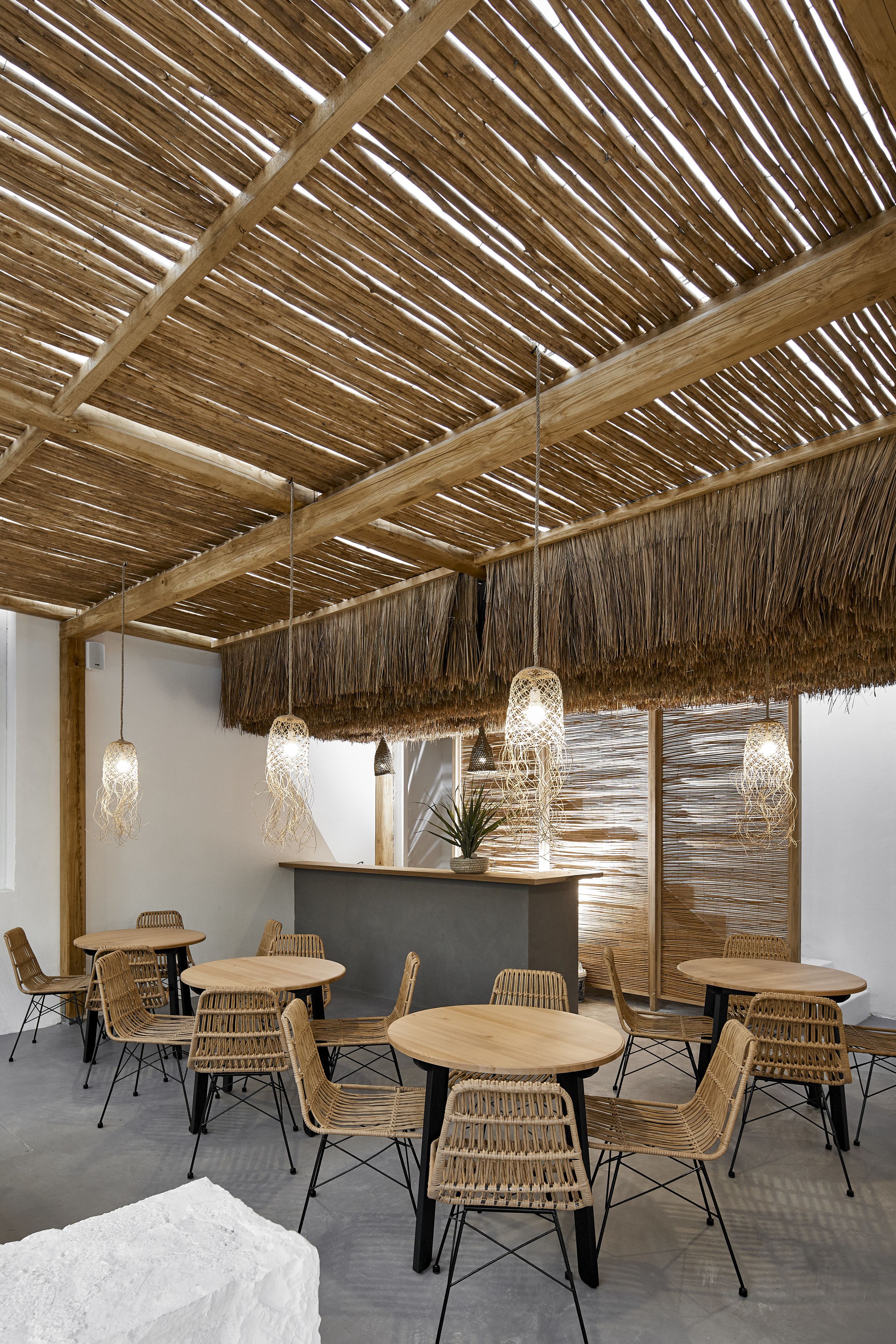 A restaurant with a thatched roof, wicker furniture, and hanging pendant lights.