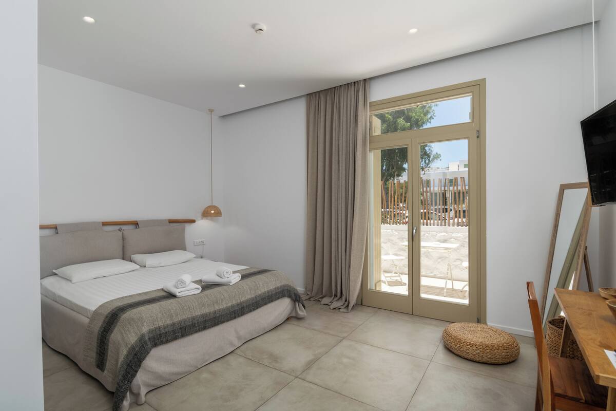 A modern bedroom with a bed, a wooden side table, a television, and a sliding glass door leading to an outdoor area.