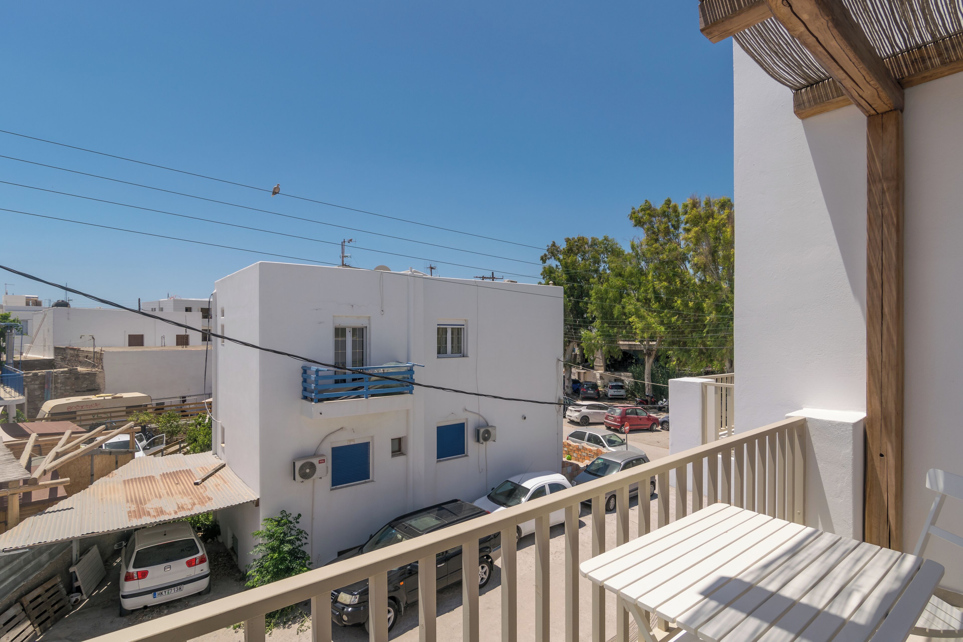 Un immeuble d’habitation doté d’un balcon, une voiture blanche garée devant, et un ciel bleu dégagé.