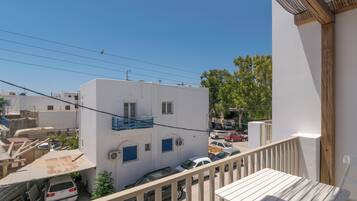 Un immeuble d’habitation doté d’un balcon, une voiture blanche garée devant, et un ciel bleu dégagé.