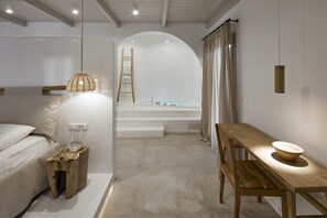 A modern bedroom with a bed, a wooden nightstand, a table with a bowl, a ladder, and a bathtub. - Arco Solium Suites (Milos)