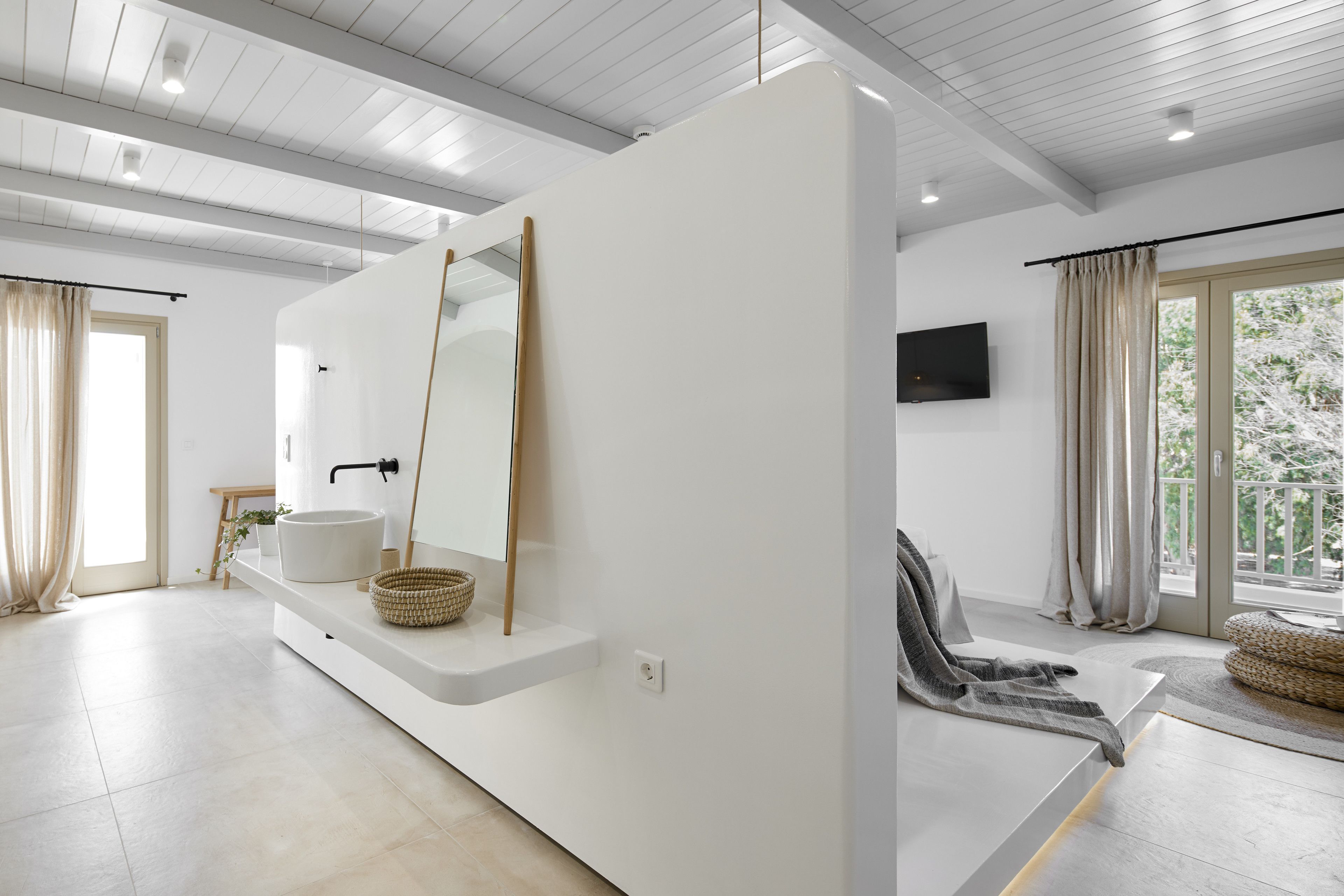 A modern bathroom with a large mirror, a white sink, and a wooden stick leaning against the wall.