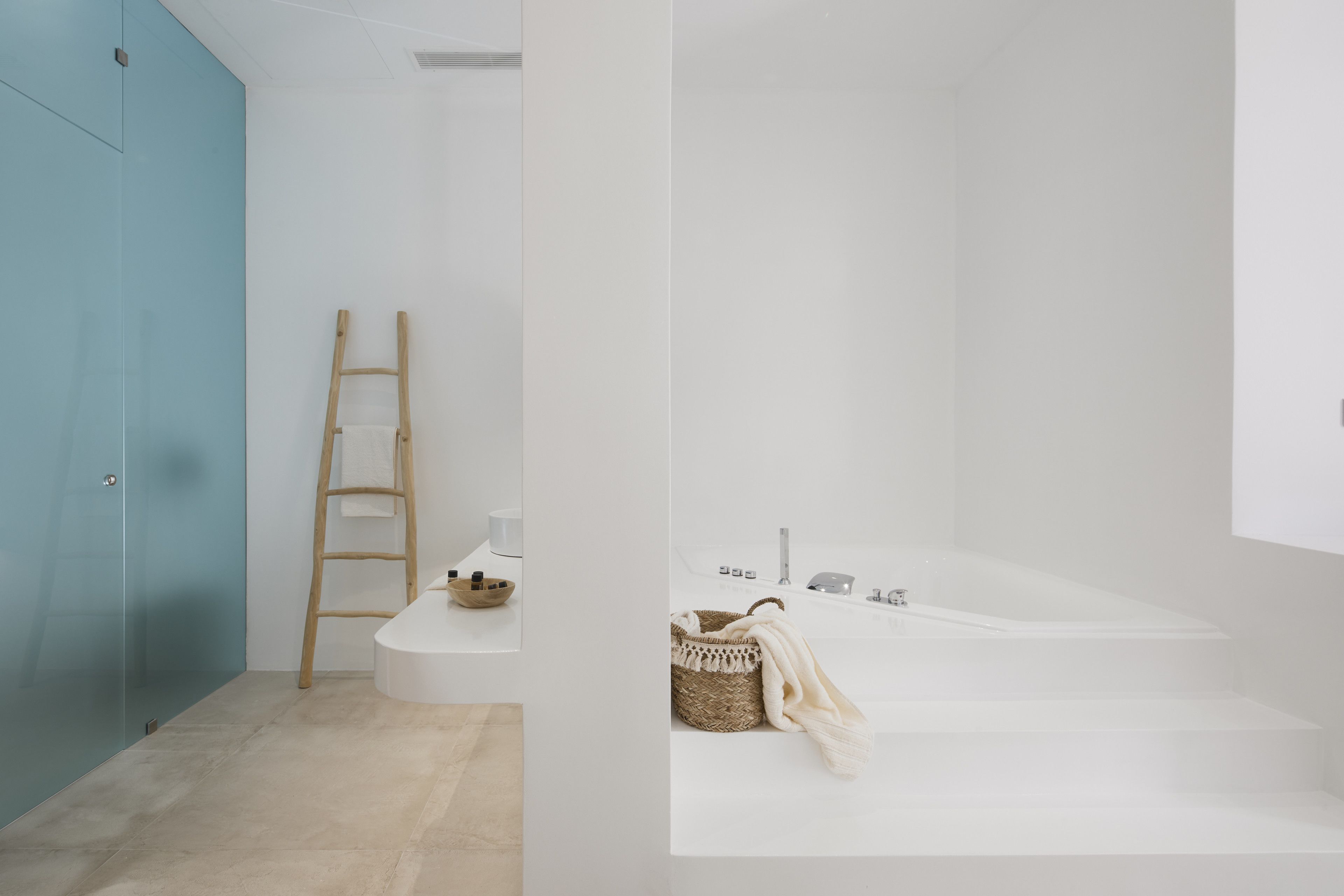 A bathroom with a blue door, a wooden ladder, a sink, a bathtub, and a woven basket with a towel.