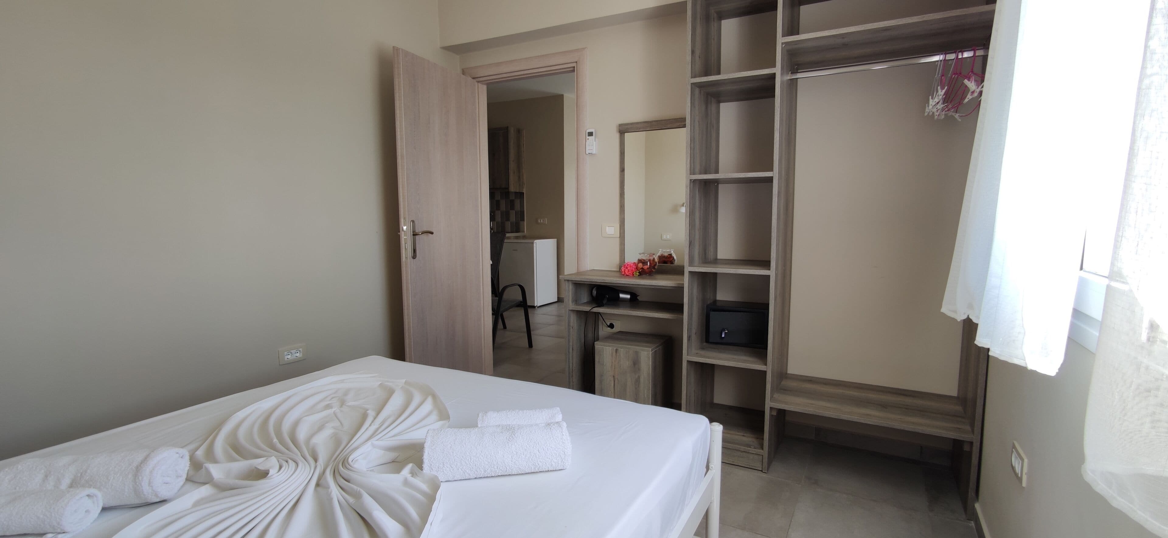 A hotel room with a neatly made bed, a wardrobe, and a desk with a computer.