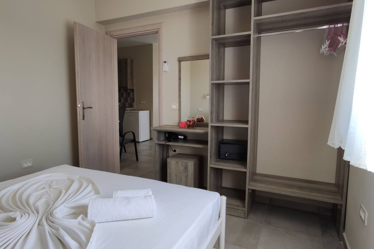 A hotel room with a neatly made bed, a wardrobe, and a desk with a computer.