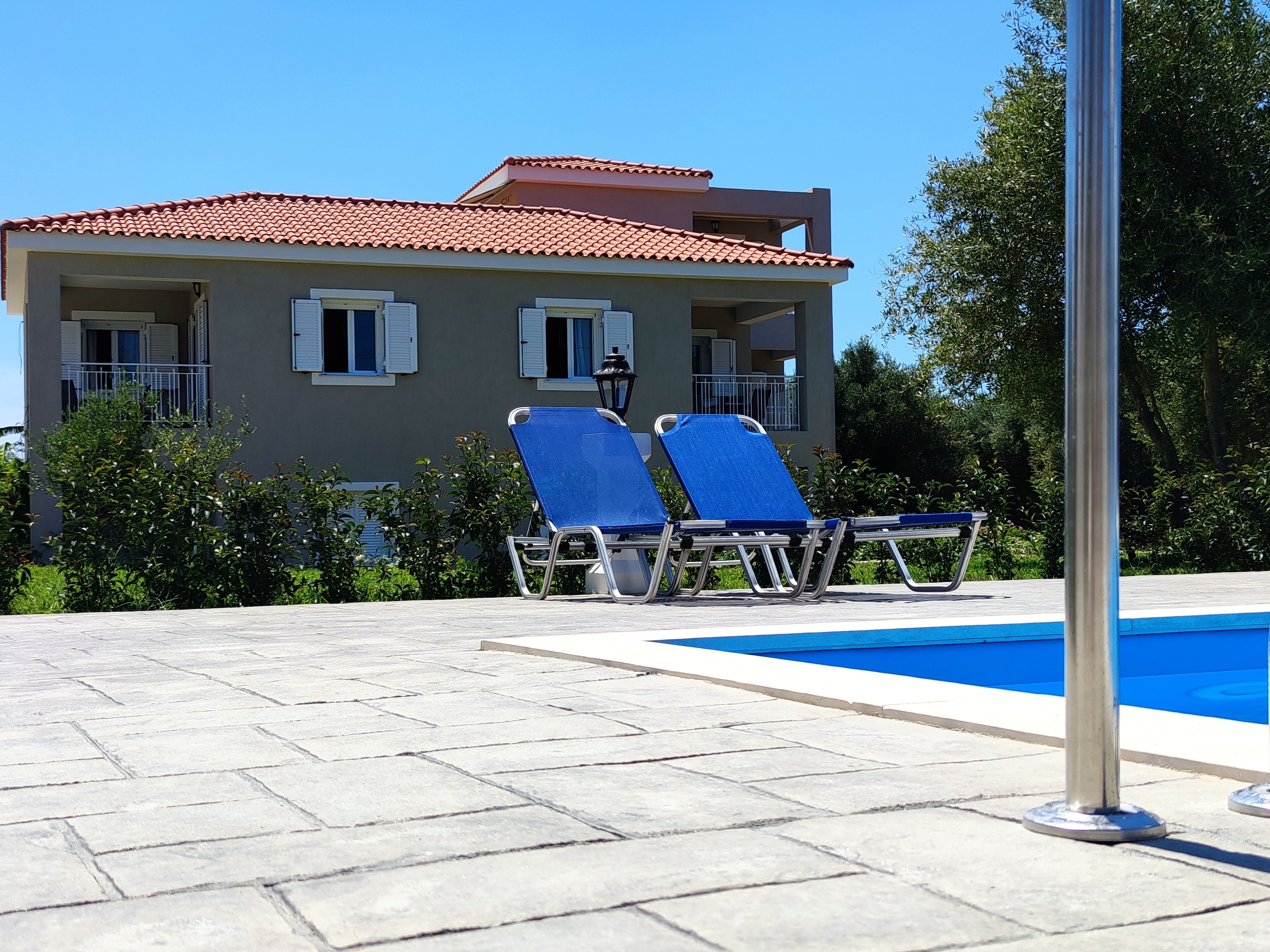 A building with a tiled roof, a swimming pool, and two lounge chairs.