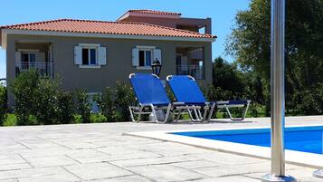 A building with a tiled roof, a swimming pool, and two lounge chairs.