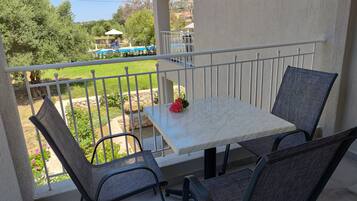 A balcony with a table and chairs, overlooking a swimming pool and garden.