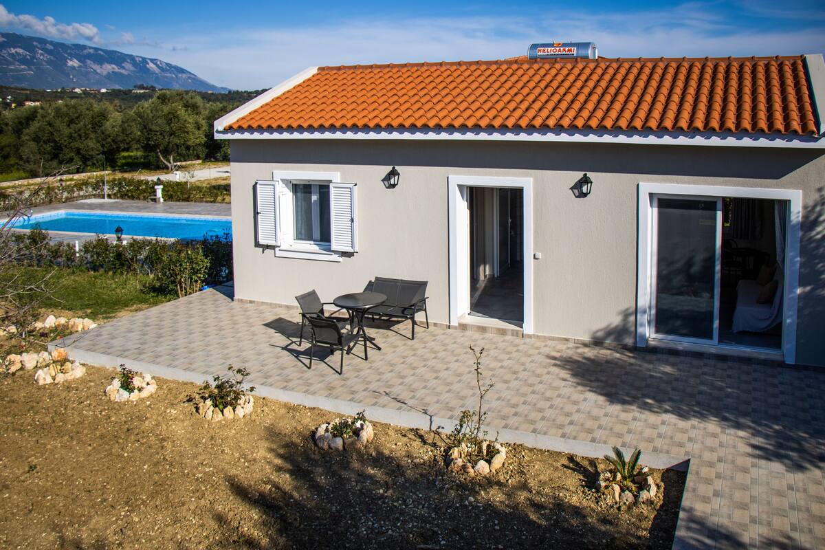 A modern house with a tiled roof, a swimming pool, and a patio with outdoor furniture.