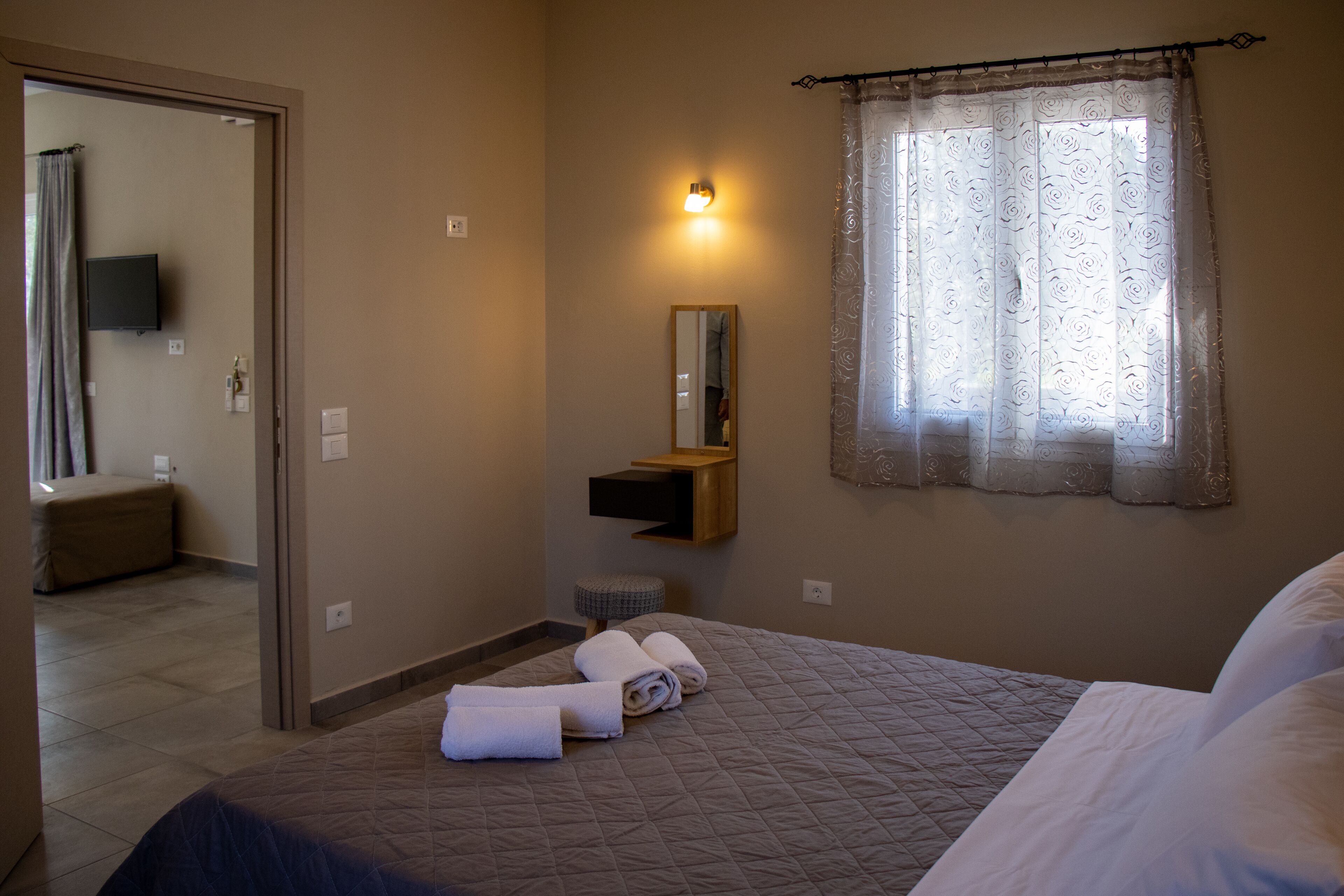 A hotel room with a bed, a bedside table, a mirror, and a window with a curtain.