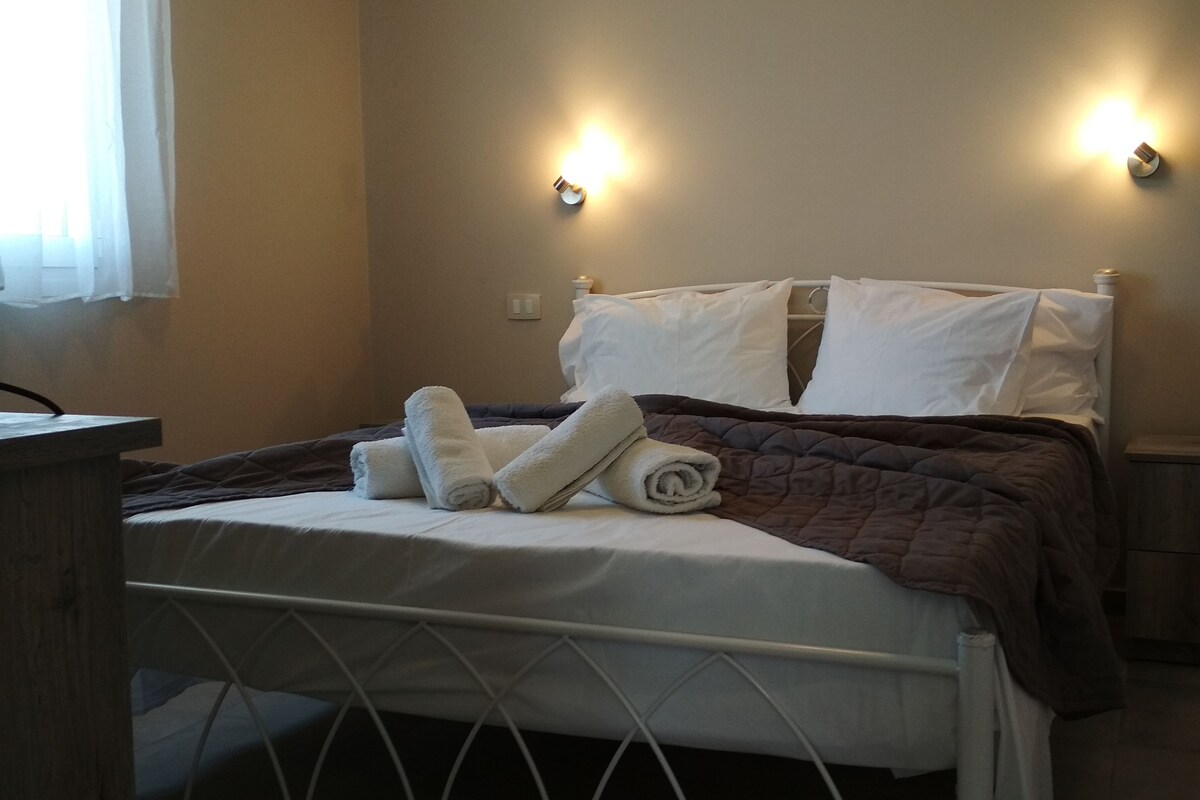 A neatly made bed with white and brown bedding, two wall-mounted light fixtures, and a small bedside table.