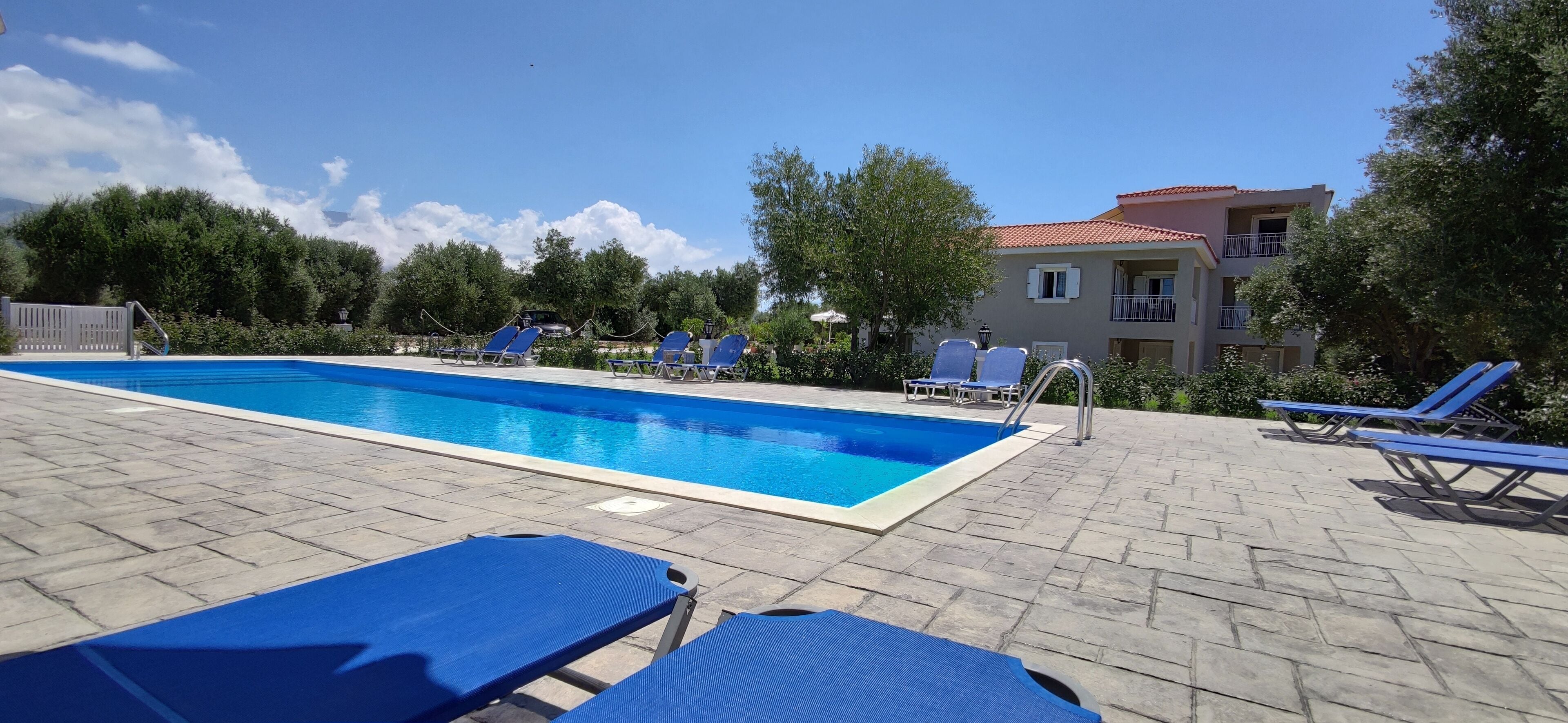 A swimming pool with blue lounge chairs and a building with a red roof in the background.