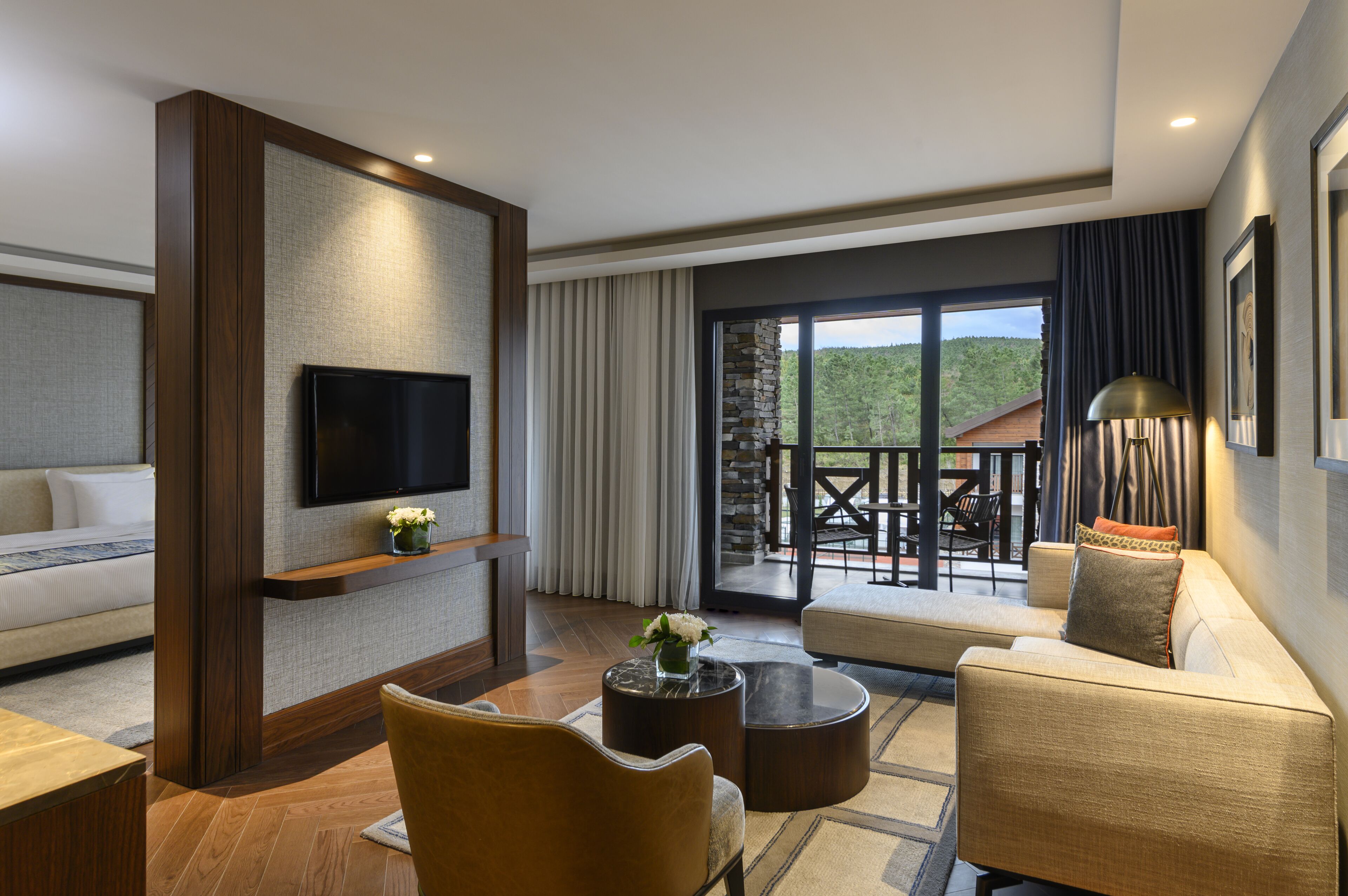 A modern living room with a flat-screen TV, comfortable seating, a fireplace, and a balcony with a scenic view.