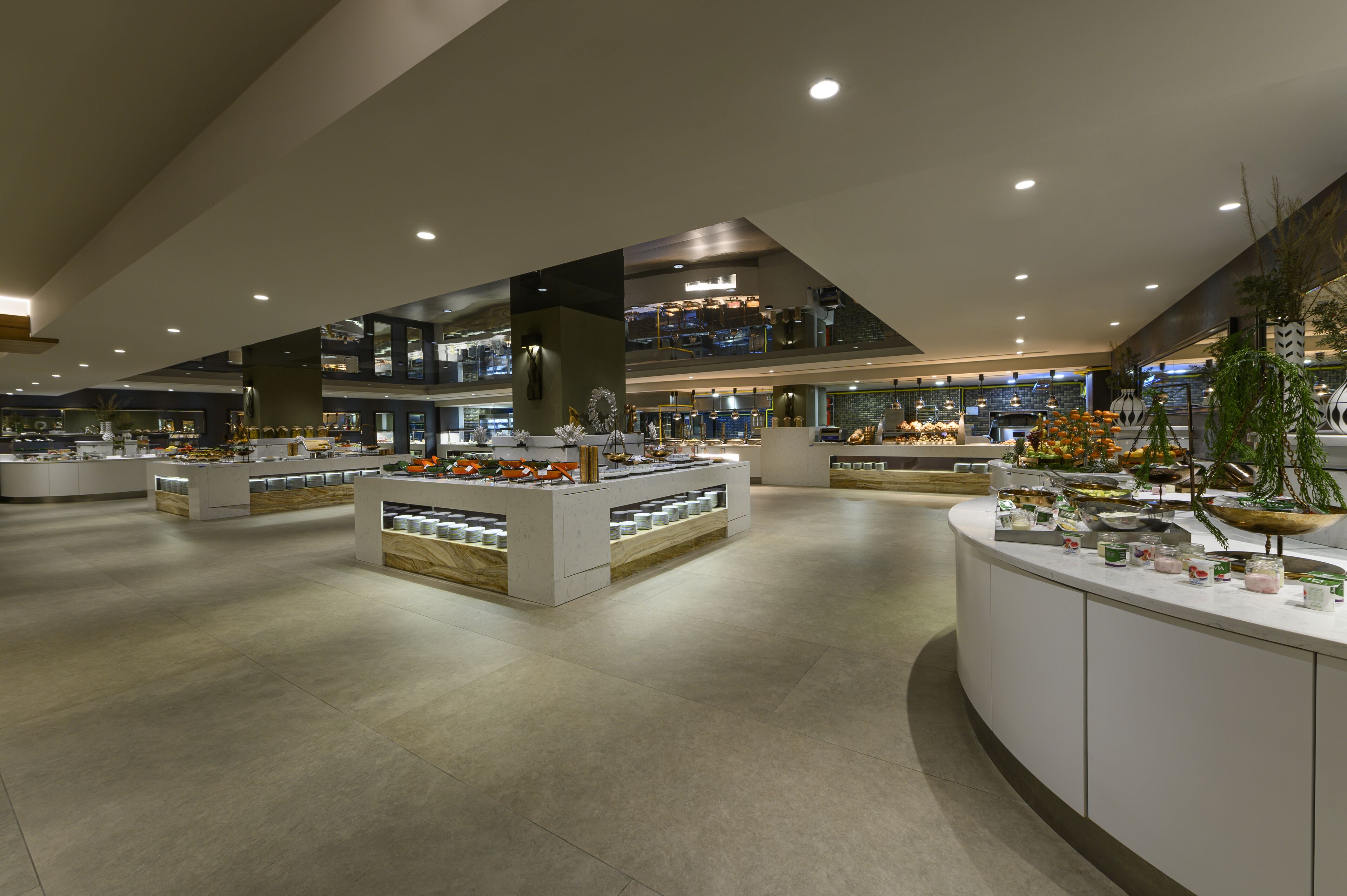 Un hall d’hôtel spacieux et moderne, doté de plusieurs espaces de détente et d’un présentoir central où sont exposés divers objets.