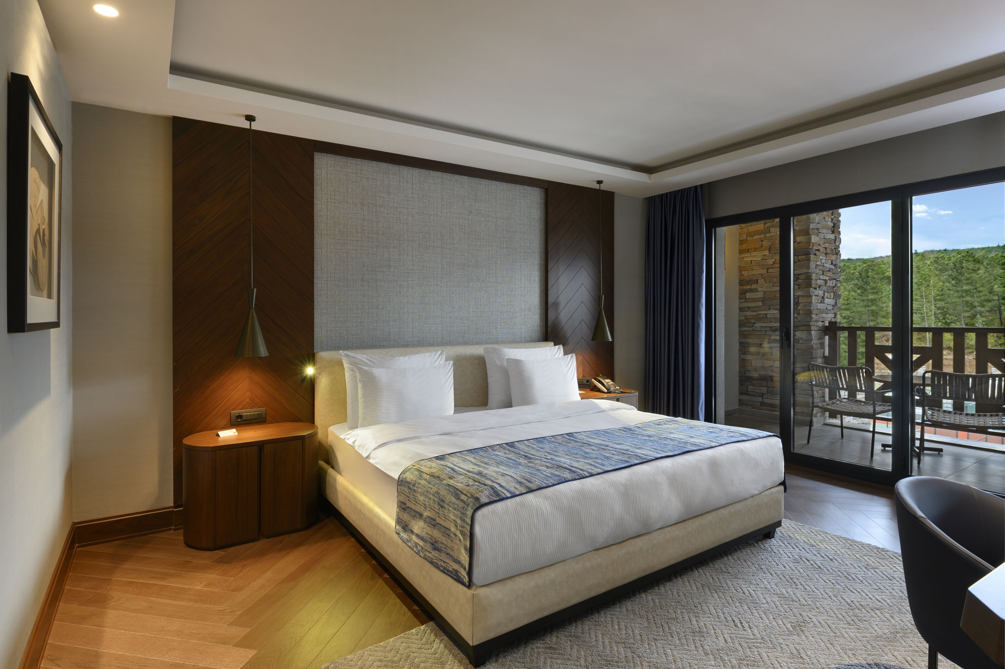 Habitación de hotel moderna con una cama grande, un escritorio y un balcón con mobiliario exterior.
