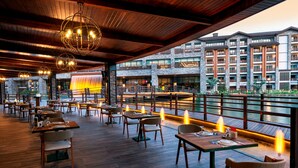 Un restaurant avec des tables et des chaises en bois, une façade en pierre et une vue sur un plan d’eau.