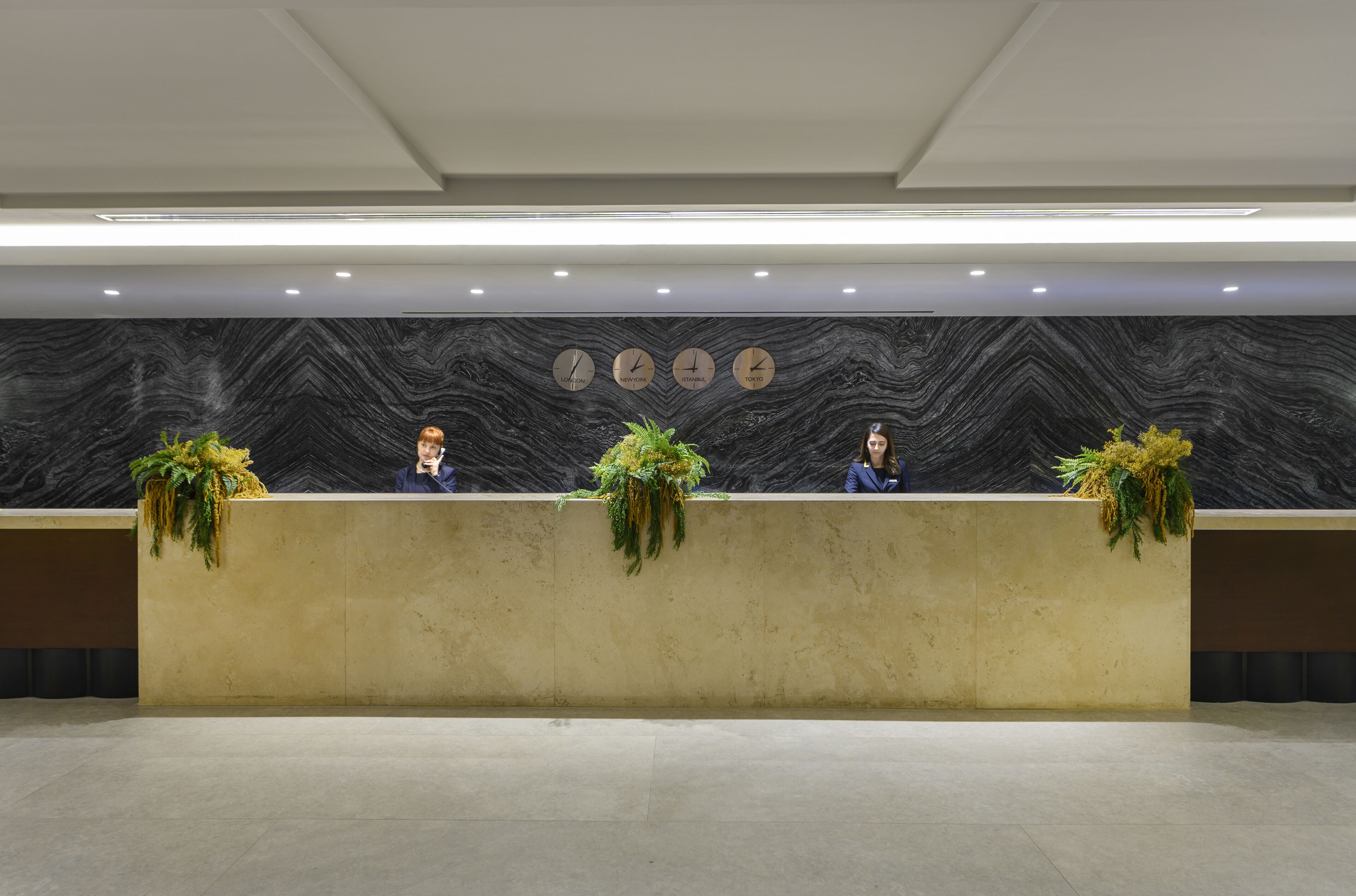 A reception desk with three staff members, each with a plant on the counter.