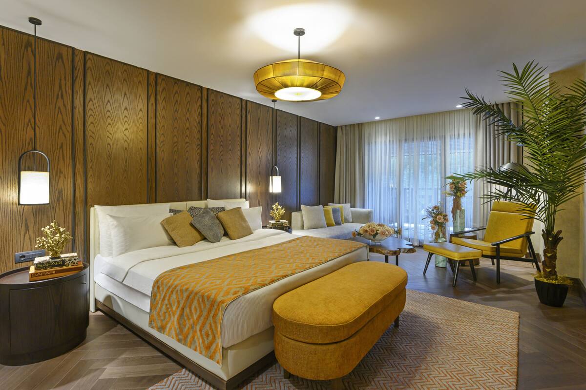 Een moderne hotelkamer met een groot bed, een zithoek met een gele fauteuil, een kleine tafel en een potplant.