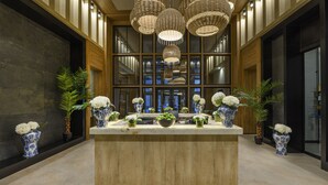 Un espace d’accueil doté d’un comptoir en bois, de vases bleus et blancs ornés de fleurs et de lustres en osier suspendus.