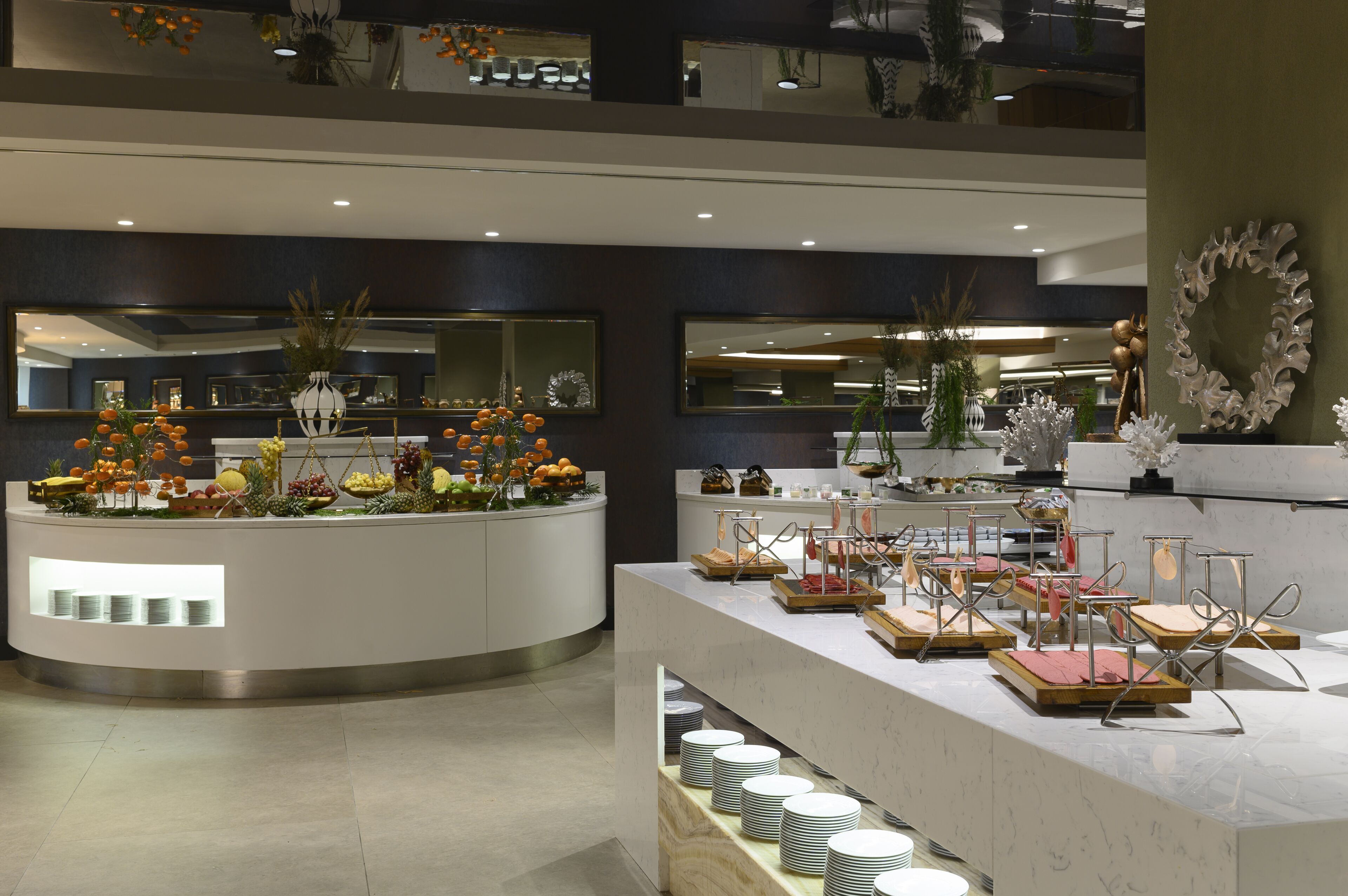 Una hall moderna di un hotel, con una reception centrale, numerosi specchi e vari elementi decorativi tra cui vasi e piante.