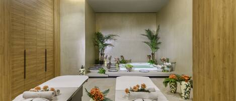 A spa room with two massage tables, a hot tub, and potted plants.