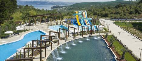 A water park with a large pool, a water slide, and a view of the surrounding landscape.