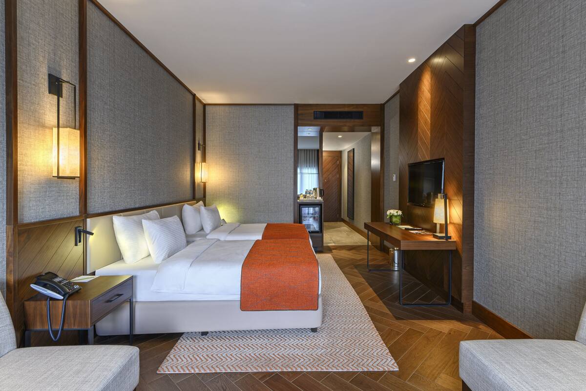Een hotelkamer met een groot bed, nachtkastjes, een bureau met lamp, een televisie en uitzicht op de hal.