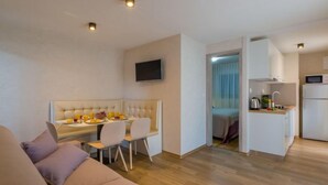 A modern living room with a sofa, a dining area with a table and chairs, and a kitchen with a microwave and sink.